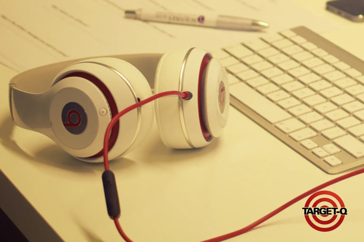 Fone de ouvido branco com cabo vermelho sobre a mesa, ao lado do teclado e de anotações de estudo